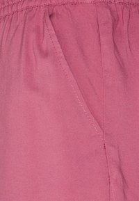 Tessuto rosa con una superficie liscia, caratterizzato da una vita arricciata e una tasca laterale. Le cuciture della cucitura sono visibili lungo i bordi.