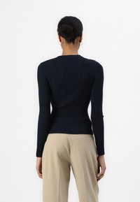 Suéter de punto acanalado en navy con mangas largas, silueta ajustada y cuello redondo, combinado con pantalones beige de tiro alto.
