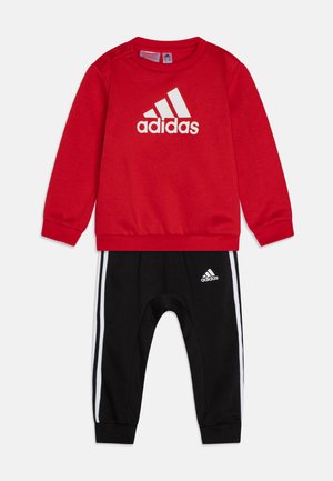 Felpa rossa con logo "adidas" bianco, collo rotondo e dettaglio con bottoni. Joggers neri con strisce bianche e piccolo logo sulla gamba.