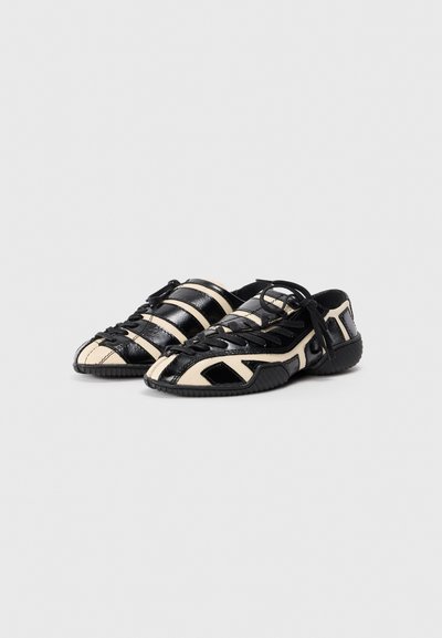 Black and cream athletic shoes with a textured upper, unique lacing, and rubber sole, featuring striped and geometric patterns.