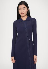 Dlhé rukávy námornícky modré šaty z rebrovanej látky, s golierom, zapínaním na gombíky vpredu a opaskom zvýrazňujúcim pás.