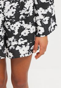 Manche et ourlet de robe à motif floral noir et blanc avec une main reposant à côté de la cuisse sur un fond uni.