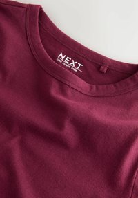 Tricou cu mânecă lungă, de culoare burgundă, cu guler rotund, fabricat dintr-un material moale. Prezintă o etichetă cu logo-ul "NEXT" și o textură subtilă. Design neted și ajustat.