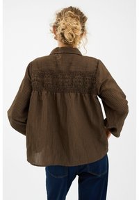 Braušais, apkakles krekls izgatavots no teksturētas auduma ar vertikālām svītrām. Aizmugurē ir savirknēta dizaina detaļa. Brīvs piegriezums ar garām piedurknēm.