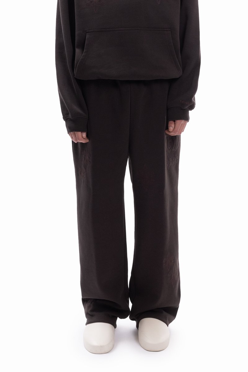 Sötétbarna kapucnis pulóver elülső zsebbel, hozzáillő bő szárú melegítőnadrággal, finom virágmintával a nadrágszárakon, fehér cipővel párosítva.