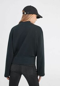 Felpa nera corta con vestibilità larga, scollatura rotonda e polsini a costina, abbinata a un cappellino nero coordinato con cinturino regolabile.