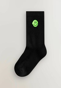 Sorte ribbede sokker lavet af tekstilmateriale, der har et neongrønt smilende ansigt-logo på ydersiden.