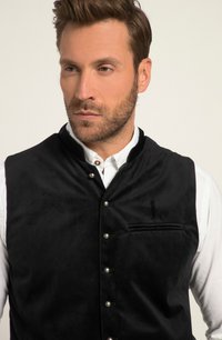 Zwarte fluwelen vest met een hoge kraag, zilveren knoopsluitingen en een borstzak, gelaagd over een wit shirt. Zachte textuur.