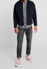 Marineblauwe corduroy jas met een bontkraag, geruite flanellen shirt, grijze jeans en roze sneakers met witte zolen.