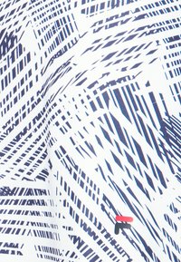 Patrón geométrico abstracto en blanco y negro con líneas y formas diagonales, que presenta un pequeño logotipo rojo y negro cerca del centro.