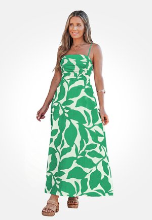 Femme portant une robe maxi sans manches à motif de feuilles vertes et blanches avec des bretelles spaghetti et des sandales plateformes tissées beiges.