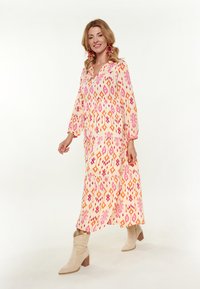 Rochie lungă, fluidă, dintr-un material ușor, cu modele vibrante de roz, portocalie și crem. Are decolteu în V și mâneci lungi; asortată cu bottine bej.