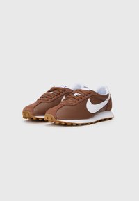 Smeđe atletske cipele izrađene od antilopa i kože, s bijelim Nike logotipom, okruglim vezicama i teksturiranom gumenom potplatom.