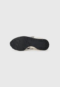 Semelle extérieure en caoutchouc noir avec un motif de traction, tige crème avec des accents gris et un détail tissé, conçue pour la durabilité et l'adhérence.