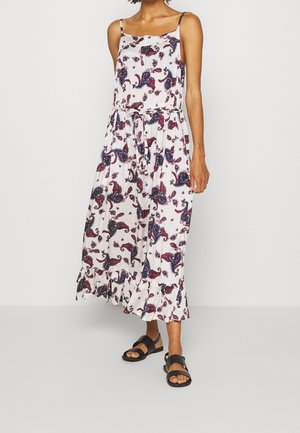 Mouwloze witte midi-jurk met paarse en roze bloemige paisleyprint, tailleband, ruches aan de zoom, gedragen met zwarte platte sandalen.