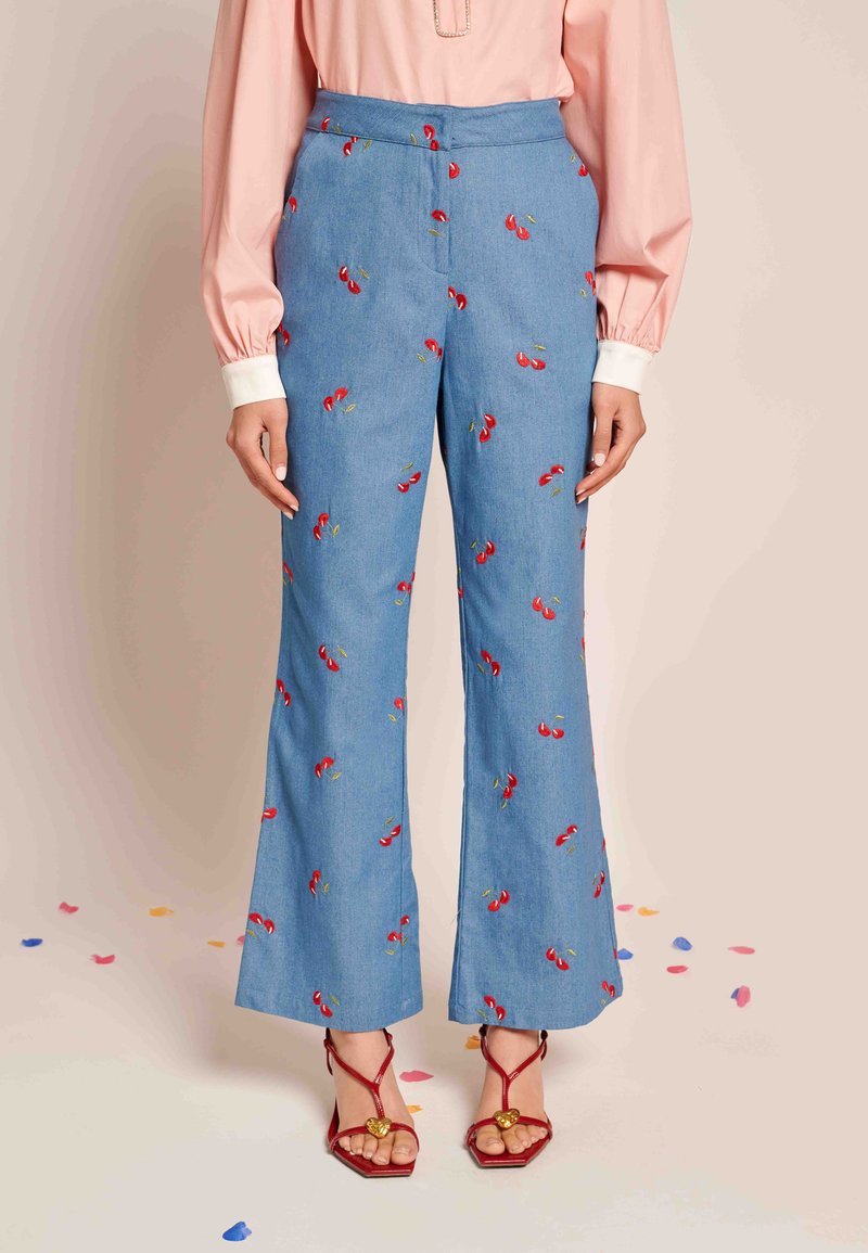 Modre kavbojke s širokimi hlačnicami in rdečimi vezeninami češenj, visokega pasu z gladko teksturo, v kombinaciji z rdečimi sandalnimi čevlji z trakovi, ki imajo zlate dodatke.