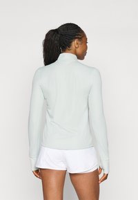 Lys blå langermet treningsgenser med høy krage, laget av teksturert stoff, tettsittende design, med tommelhull, sammen med hvite shorts.