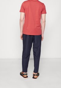 Röd bomulls-t-shirt, marinblå byxor och svarta sandaler med orangea accenter. Outfiten har en avslappnad passform och enkel design.