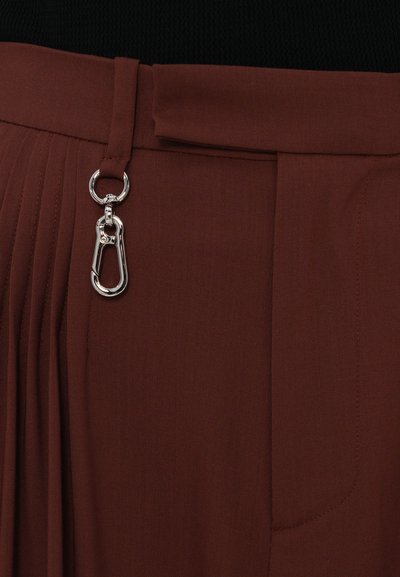Pantaloni crem plisati cu o textură netedă, având un clip metalic și o buclă pentru prindere, concepuți cu un brâu pentru o ajustare sigură.