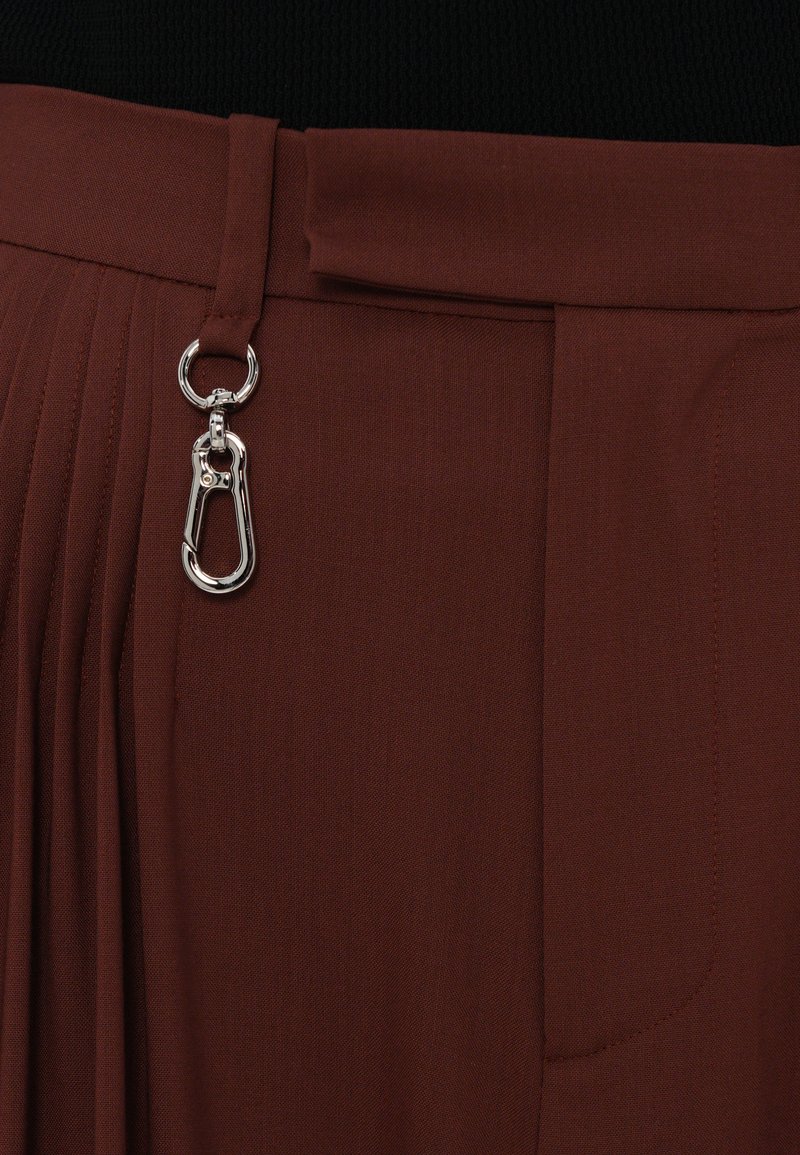 Brune plisserede bukser med en glat tekstur, udstyret med en metalclips og sløjfe til lukning, designet med en talje for en sikker pasform.