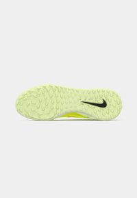 Podeszwa żółtego korka piłkarskiego z teksturowanym gripem i czarnym logo Nike na jednolitym białym tle.