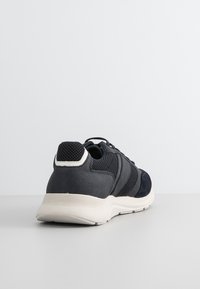 Scarpa atletica blu scuro caratterizzata da un mix di materiali in rete e pelle, silhouette arrotondata, accenti testurizzati e suola in gomma bianca.