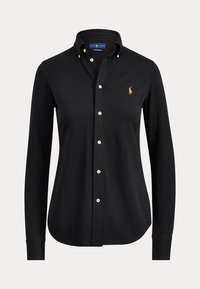 Chemise noire à manches longues, boutonnée avec col et boutons blancs, arborant un petit logo brodé d'un joueur de polo sur la poitrine gauche.