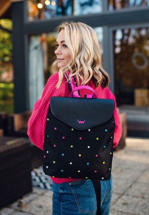 Black backpack with colorful polka dots, a rounded flap, and pink straps. Material appears durable fabric, design includes a logo on the flap.