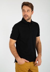 Zwarte polo met korte mouwen, en een placket met drie knopen en een subtiele logodetail. Zacht, effen materiaal met een klassieke pasvorm.