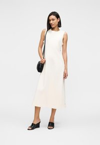 Κρεμ midi φόρεμα χωρίς μανίκια με άνετη εφαρμογή, λεία υφή και ελαφρώς γραμμή A. Συνδυασμένο με μαύρα mules με χοντρό τακούνι και μικρή τσάντα.