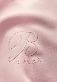 Jasnoróżowa tkanina o gładkiej strukturze, z wytłoczonym logo stylizowanej litery "B" oraz słowem "BAKER" pod spodem w nieco ciemniejszym odcieniu.
