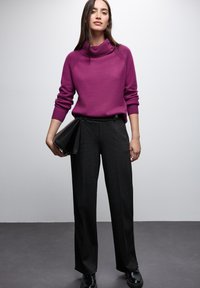 Fioletowy sweter dzianinowy z szerokim dekoltem, luźny krój i detal w postaci dwóch guzików. Szare dopasowane spodnie, wysokiej talii, szerokie nogawki, zestawione z czarną kopertówką.