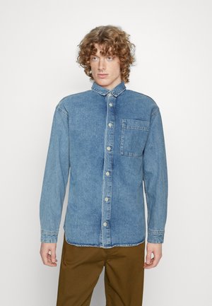 Camicia in denim azzurro chiaro con chiusura a bottoni, colletto a punta e una tasca sul petto. Le maniche lunghe presentano polsini. Tessuto liscio.