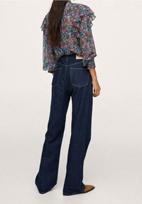 Blomstret bluse med flæser i forskellige farver, parret med mørkeblå, bred ben denim jeans. Jeansene har høj talje og baglommer.