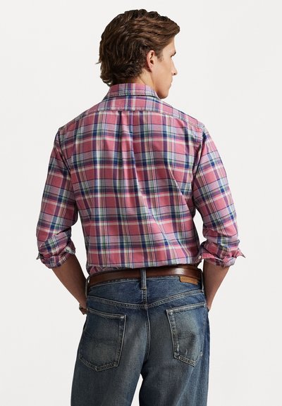 Sjekkrutet skjorte i rosa, blå og grønn med oppbrettede ermer, kombinert med mørk denimjeans med baklommer og et brunt belte.