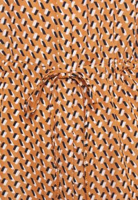 Brunt tyg med ett geometriskt mönster av svarta och vita rektanglar, knutet i midjan med ett matchande bälte. Služ yta.