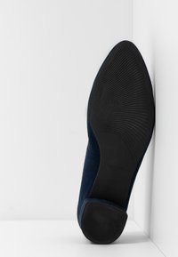 Chaussure à talon haut en daim bleu marine avec un bout pointu, dotée d'une semelle en caoutchouc noire texturée et de côtés lisses.
