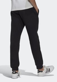 Svarta sweatpants av mjukt material med sidofickor och ribbade ärmslut, i kombination med vita sneakers med svarta ränder och logotyp.