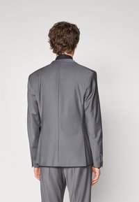Grå dressjakke sett bakfra, med slim fit, klaffeslag og subtil tekstur. Skreddersydd design med kontrastfarge på kragen.
