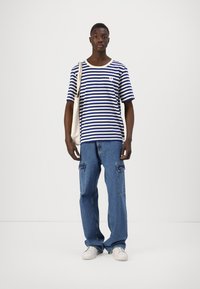 Camiseta de rayas azul y blanca de manga corta con cuello redondo, combinada con pantalones vaqueros holgados de color azul claro con bolsillos tipo cargo y zapatillas blancas.