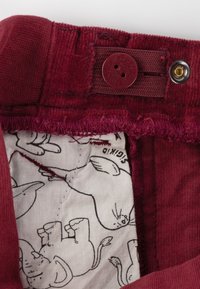 Burgunderfarbener Baumwollbund mit Knopfverschluss und Futter, das ein verspieltes Tiermuster in Schwarz auf hellem Hintergrund zeigt.