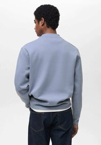 Felpa azzurra chiara realizzata in tessuto misto cotone, con scollatura rotonda e polsini a coste, mostrata da dietro con jeans scuri.