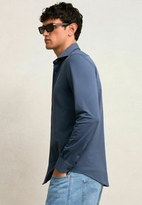 Langärmliges, knöpfbares Hemd in einheitlichem Marineblau, aus glattem Stoff mit spitzem Kragen und Manschetten, kombiniert mit hellblauen Jeans.
