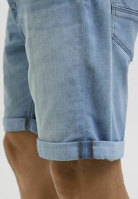 Lysblå denimshorts med opfoldede kanter, der har en glat tekstur og subtile stikninger langs siden og sømmen.