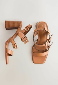 Sandales à talons marron avec un bout carré, plusieurs bandes réglables et des boucles en ton or. Le talon présente un design texturé et rayé.