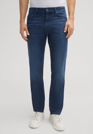 Dark blue denim jeans with a straight fit, five pockets, and subtle fading. Paired with white athletic shoes.