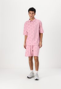 Pink short-sleeve polo and matching shorts with a textured pattern. The fabric appears soft, with a slight sheen. Worn with white athletic shoes.