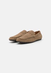 Brązowe zamszowe mokasyny ze szwowym noskiem, płaską gumową podeszwą oraz dekoracyjnym akcentem z boku. Czyste linie i elegancki design.