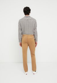 Καρό γκρι και λευκό πουκάμισο με κουμπιά, χακί παντελόνι και λευκά αθλητικά παπούτσια. Στενή εφαρμογή με λεπτομέρειες πίσω τσέπης και διακριτική σήμανση.