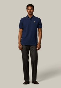 Granatowa koszulka polo z krótkim rękawem, kontrastowym kołnierzykiem i emblematem. Połączona z dopasowanymi spodniami w odcieniu węgla i ciemnymi butami.